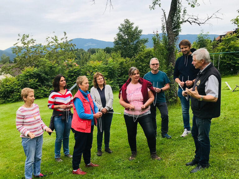 Fröhliche Personen in bunter Freizeitkleidung genießen die Natur auf der Wiese mit einer Wünschelrute.